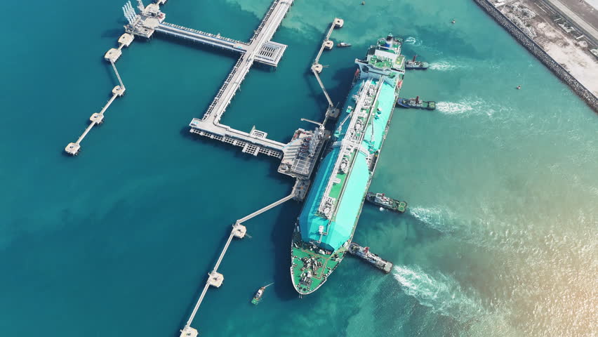 large green LNG tanker ship being assisted by tugboats at a maritime terminal in the Strait of Hormuz. Global energy logistics and international natural gas trade today.