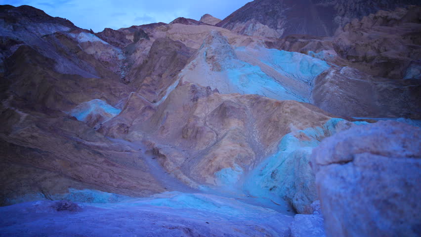 Artist Panel, Death Valley National Park. Dramatic twilight scene reveals colorful desert mountain formations with striking blue and orange mineral deposits. Rocky terrain displays vibrant hues 