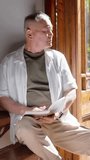 Vertical video: Light drawing senior glancing at door and book, turning pages on bench in white tee. Portrait, minimalist, serene, sunlit, garden, journal, vertical video - Powered by Shutterstock - Get 15% off with code: PIKWIZARD15