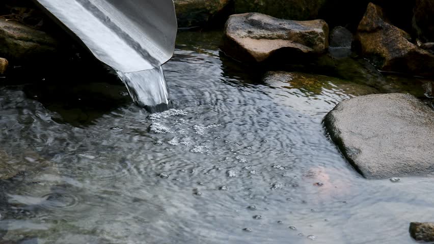 A forest spring with clear and clean water. A small, gentrified spring running down the rocky surface into the pool below. Water flows over moss-covered rocks.