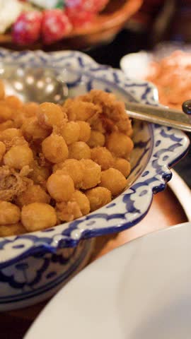 Close-up shot of a hand using a spoon to serve fried shrimp balls onto plates