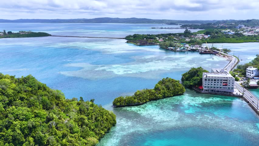Drone footage captures turquoise water, coral reefs, and a coastal hotel under bright daylight