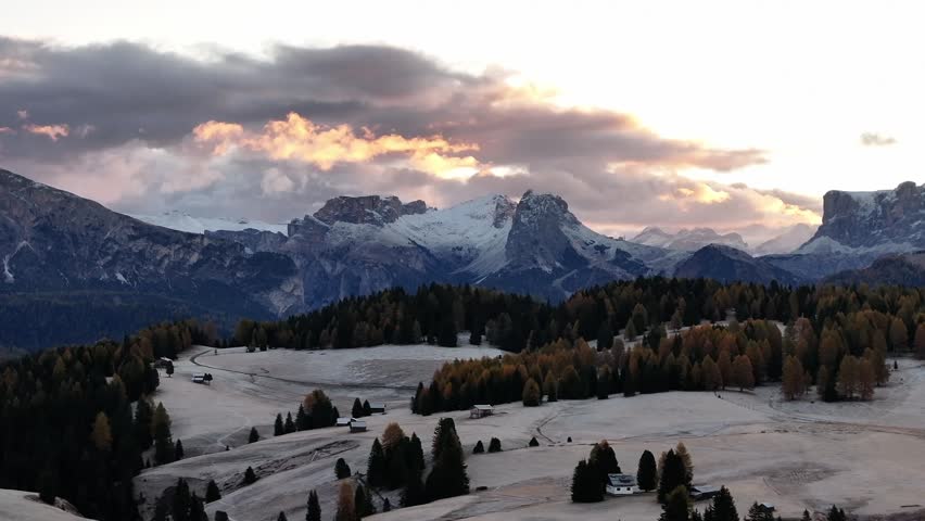 Stunning drone view of the Sassolungo mountain range, Langkofel in the Dolomites. Majestic alpine peaks covered in light snow, autumn colored forest all around, and yellow grass covered in morning white hoarfrost. Picturesque natural landscape