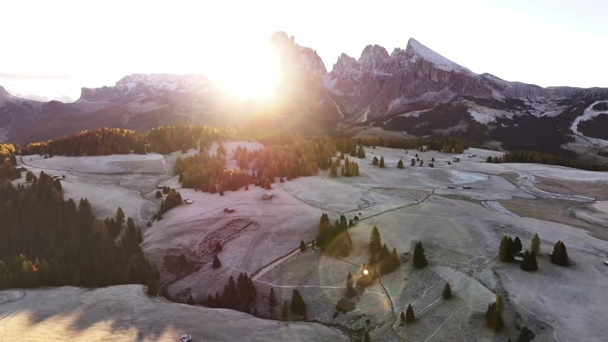 Stunning drone view of the Sassolungo mountain range, Langkofel in the Dolomites. Majestic alpine peaks covered in light snow, autumn colored forest all around, and yellow grass covered in morning white hoarfrost. Picturesque natural landscape