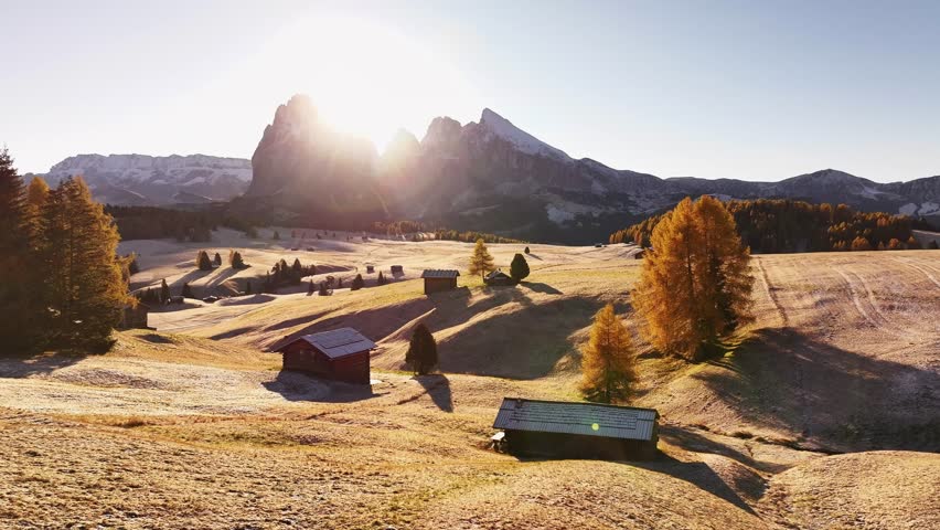 Stunning drone view of the Sassolungo mountain range, Langkofel in the Dolomites. Majestic alpine peaks covered in light snow, autumn colored forest all around, and yellow grass covered in morning white hoarfrost. Picturesque natural landscape