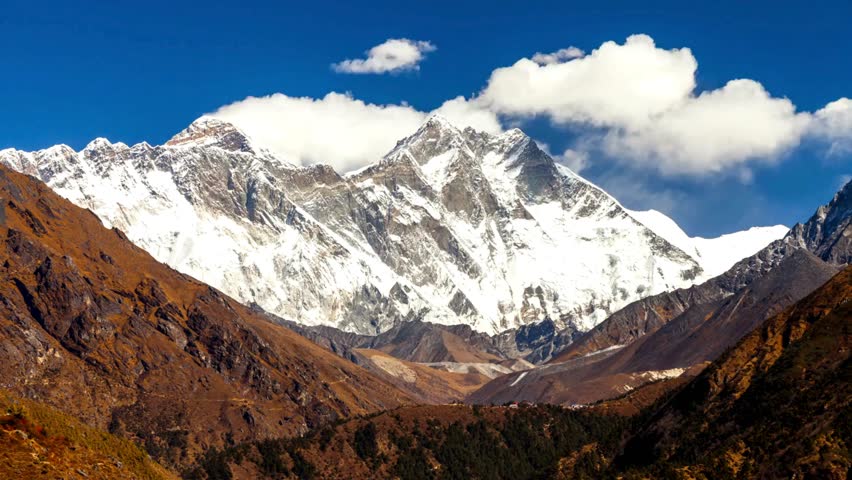 Snow-covered peaks rise dramatically in the Himalayas of Nepal. Lush green valleys and rugged terrain create a breathtaking mountain landscape under bright skies.