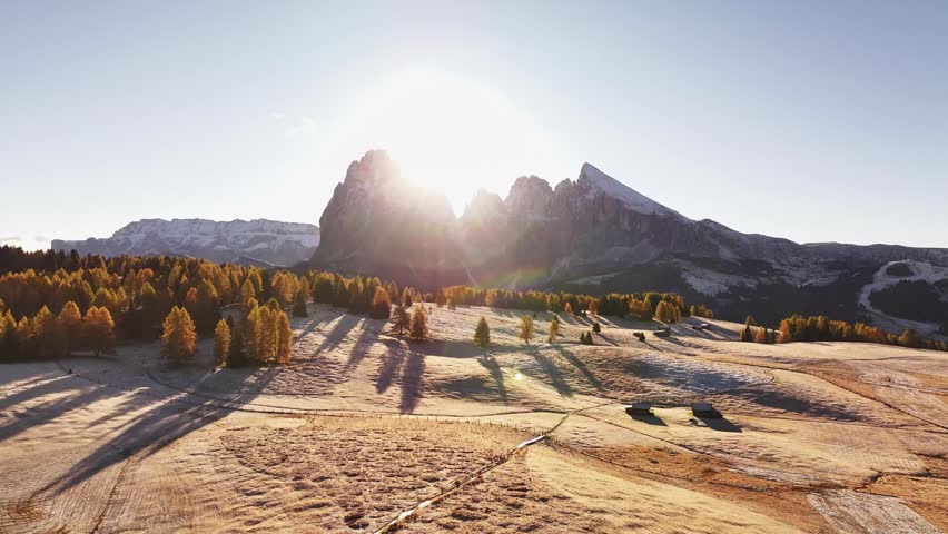 Stunning drone view of the Sassolungo mountain range, Langkofel in the Dolomites. Majestic alpine peaks covered in light snow, autumn colored forest all around, and yellow grass covered in morning white hoarfrost. Picturesque natural landscape
