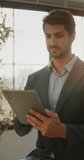 Portrait of Hispanic businessman smiles as holds tablet in office near window during workday. Man looks at camera and reviews project notes on screen vertical - Powered by Shutterstock - Get 15% off with code: PIKWIZARD15