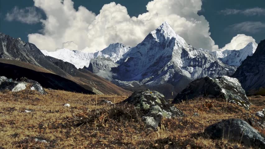 Explore a breathtaking mountain landscape where snowy peaks tower over rocky terrain. The clear sky and dramatic clouds create a stunning backdrop for nature