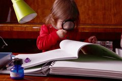 Little baby girl studies books and texts using a magnifier lens. Suitable for educational videos and similar.
