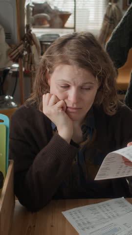 Vertical shot of man supporting wife, comforting her at table with unpaid documents, going through hardship together