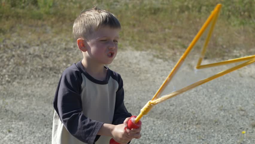 Boy creating large soap bubbles in outdoor setting with toy, child activity concept for lifestyle and family marketing visuals. Soap bubbles highlight play, movement and creative development. 