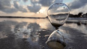 An hourglass on the beach with gentle waves flowing around it at sunset. Concept of passing time, fleeting moments, life transition, and time management. 4K slowmotion footage. - Powered by Shutterstock - Get 15% off with code: PIKWIZARD15