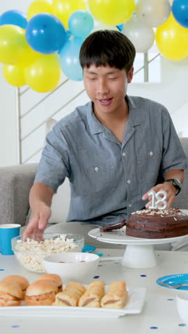 Vertical video: Asian teenager grabbing popcorn scooping nuts on sofa, eating cake at 18th birthday. Celebration, friendship, party, festive, domestic, casual, vertical video