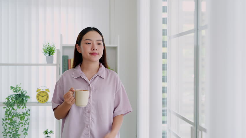 Woman in pajamas holding coffee cup looking out window.