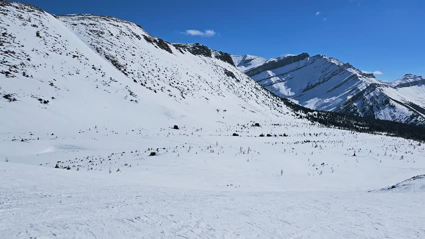 Scenic ski slopes in Banff National Park overlook a snowy alpine valley surrounded by rugged Canadian Rockies peaks.