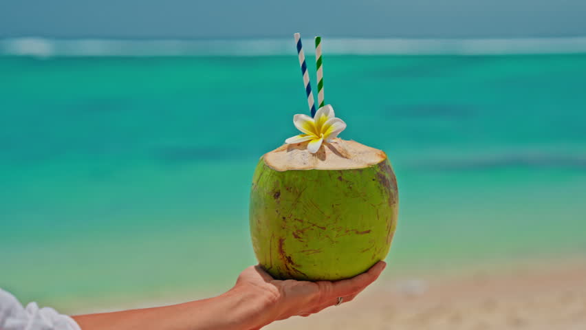 A close-up portrait of a woman drinking a fresh coconut cocktail with turquoise water on the shore of the Indian Ocean. A smile on the face. Positive emotions. Concept of relaxation and travel