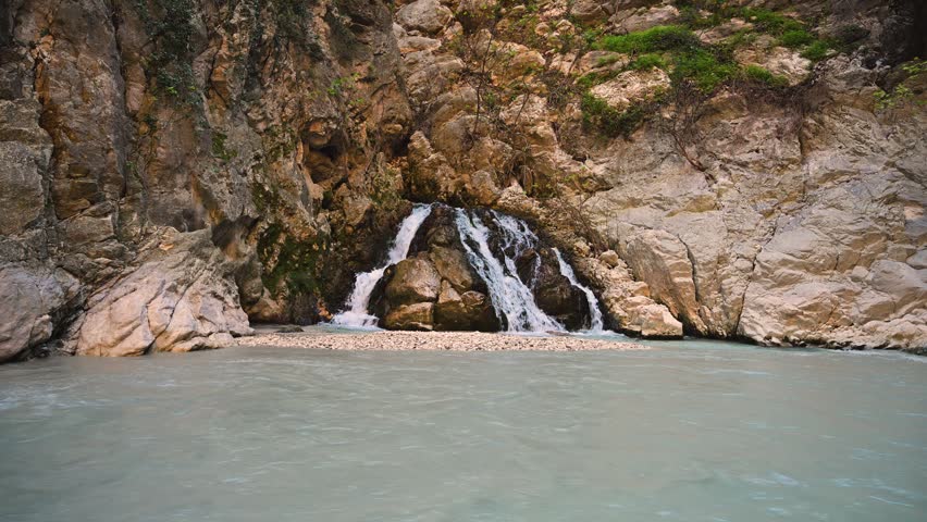 Stunning natural landscape showing a small waterfall flowing over rocks into a calm river at the bottom of the impressive Saklikent Canyon