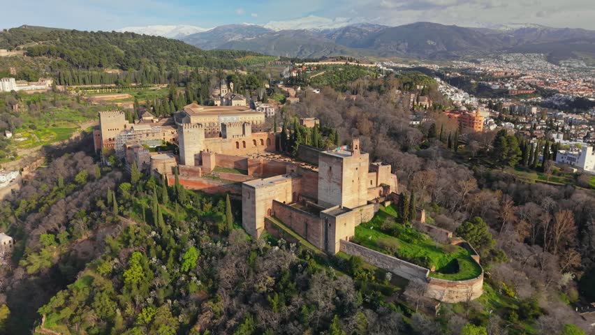 Aerial view of majestic Alhambra fortress in Granada, ancient Moorish palace stands beautifully against backdrop of snowy mountains. Alhambra palace complex at sunrise. Granada citadel in Spain