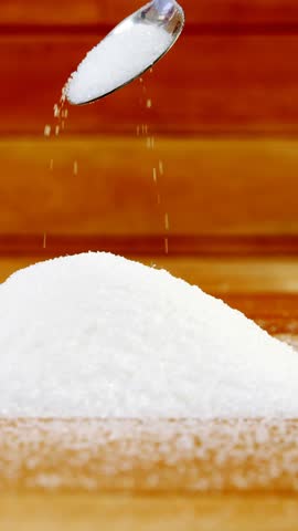 Sugar pouring from spoon on a wooden table 4k