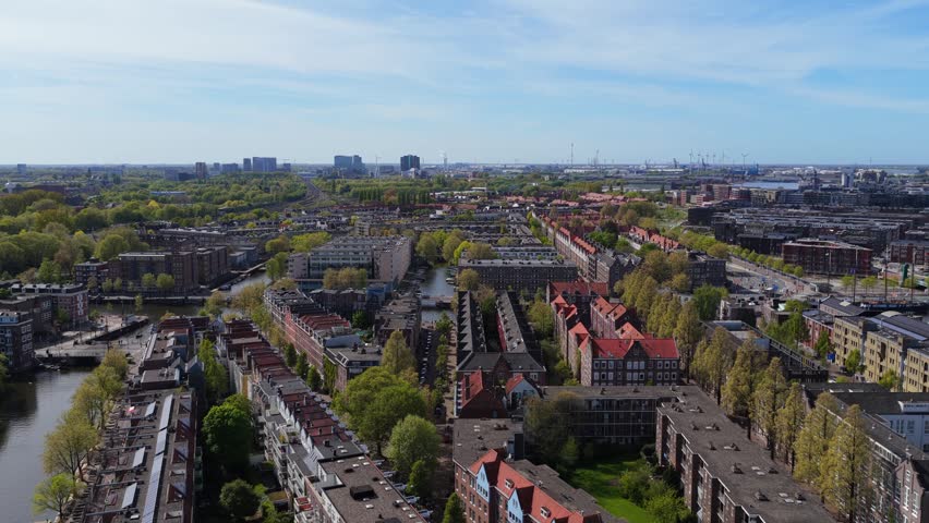 Amsterdam suburban residential area with Spaarndammerbuurt district, green trees, canals, Westerpark from above on sunny day in Netherlands with city skyline