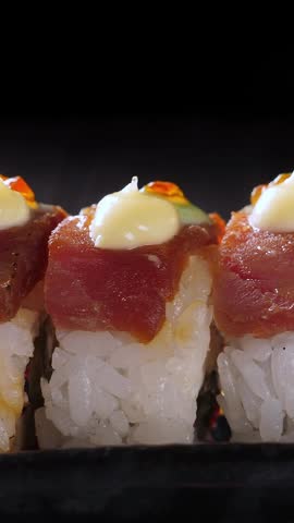 Sushi rolls with tuna adorned with roe on black platter. Vertical footage