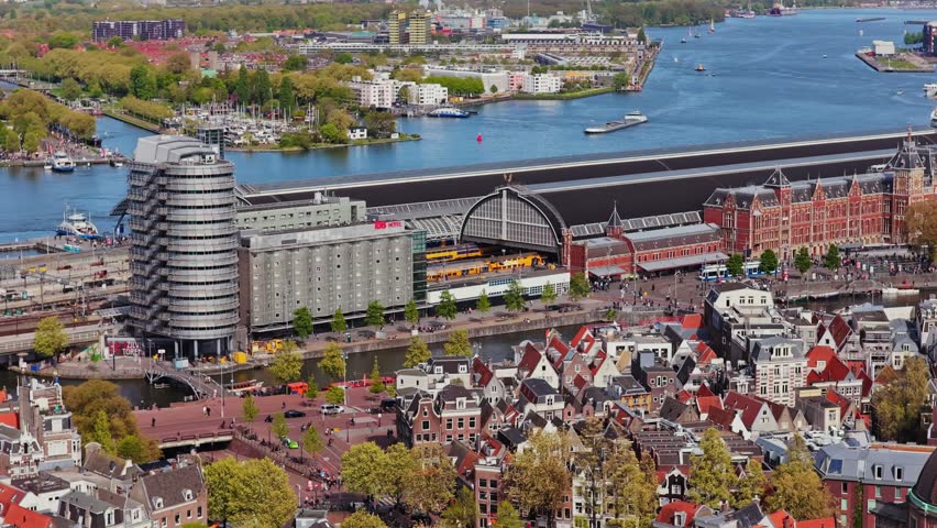 Amsterdam Centraal Station aerial revealing Netherlands historic city architecture and busy water transport on IJ river during a sunny spring day in capital city
