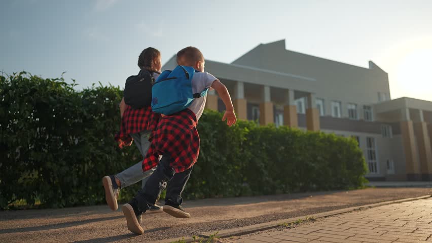 Girl and boy students carry backpacks as they walk toward school building. Morning light touches their path. Each backpack bounces slightly as student girl walks beside child boy on morning walk