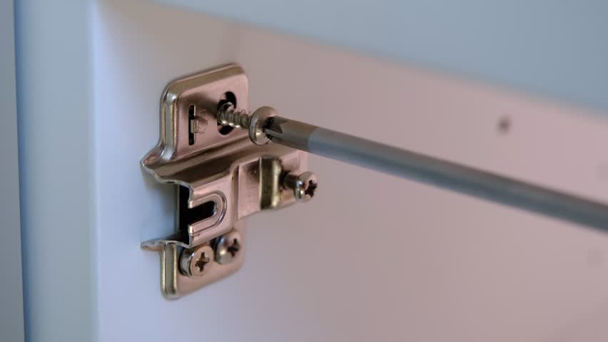 Close-up of a worker screwing a hinge mounting plate into a furniture panel