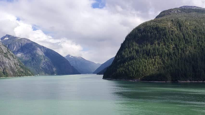 Tracy Arm, USA - A mesmerizing view of Tracy Arm Fjord, Alaska. The waterway is surrounded by towering mountains blanketed with verdant forests. The waterway extends into distant mountain ranges.