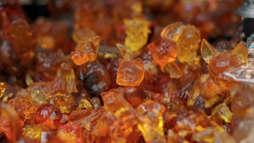 Amber animal figurines displayed at a market stall. Collection of small carved orange resin trinkets and jewelry souvenirs. Natural fossilized gemstone art craft.