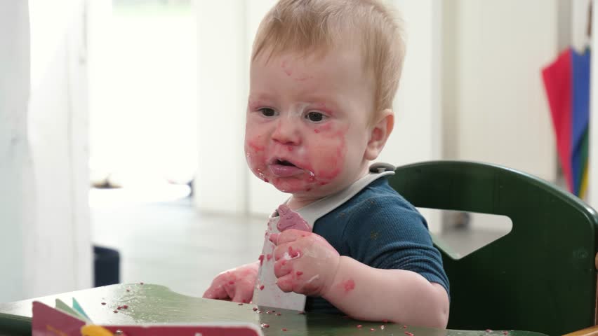 Messy Infant indulges in sweet treat during mealtime. Curious baby eating cookie at home in high chair