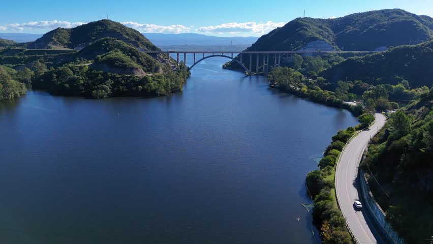 Sunny aerial landscape showing the jose manuel de la sota bridge spanning san roque lake in cordoba, argentina, with traffic on a nearby road