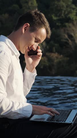 Lakeside Business Call While Typing Caucasian Man, White Shirt Executive Balancing Phone And Laptop, Candid Profile, Animated Conversation, Remote Meeting Vibe, Travel Workspace, Urgent Multitasking,