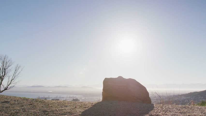 Female runner passing rock on sunlit hilltop, activating technology overlay for network demo. Silhouette, athlete, outdoor, landscape, horizon, ridge, boulder