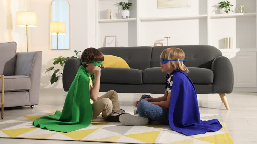 Little boys in superhero costumes playing rock, paper and scissors at home