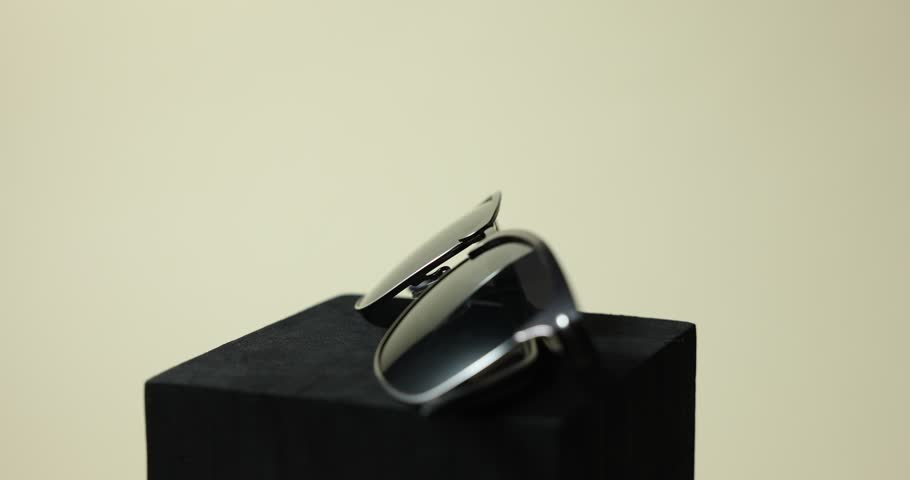 Pair of stylish sunglasses on podium against light background, rotating