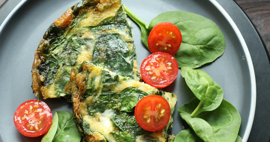 Tasty omelette with spinach and tomatoes on wooden table, spinning. Closeup view