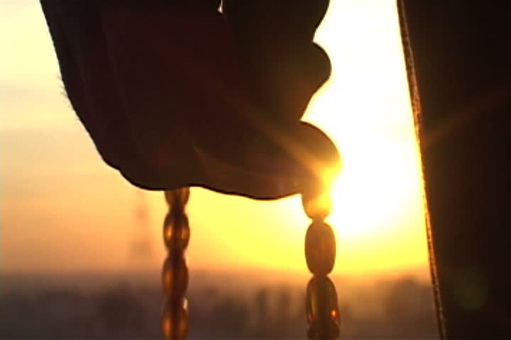 Silhouette of hand counting off prayer beads with bright orange setting sun in background in Mosul, Iraq. | Shutterstock HD Video #4064290