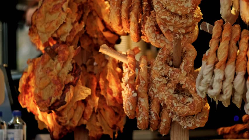 Golden pretzel hanging on wooden rack at market stall. Fresh baked pastry with almond and white glaze. Sweet snack product for Christmas fair shopping experience.