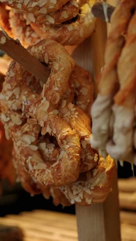 Golden pretzel hanging on wooden rack at market stall. Fresh baked pastry with almond and white glaze. Sweet snack product for Christmas fair shopping experience.