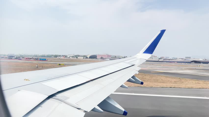 Airplane taking off from Mumbai airport seen from window seat. Runway and city visible during ascent.