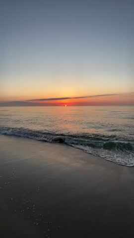 Beautiful sunset over the calm ocean waves hitting the sandy beach in the evening