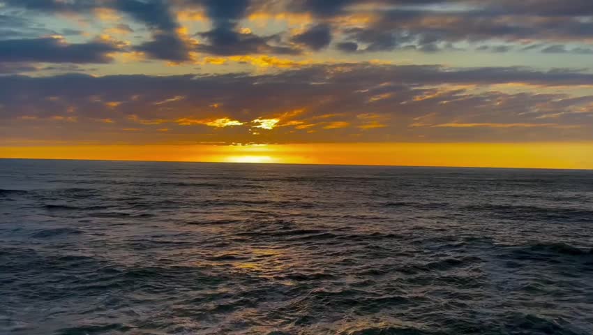 Beautiful golden sunset over the calm dark ocean water with clouds in the sky