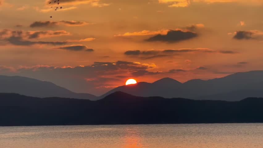 Beautiful orange sunset over dark mountain range and calm lake water in the evening