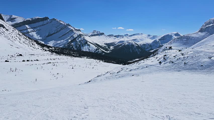 Banff, Canada ski mountain panorama shows fresh snow, distant peaks, and a vast winter valley beneath a bright blue mountain sky.