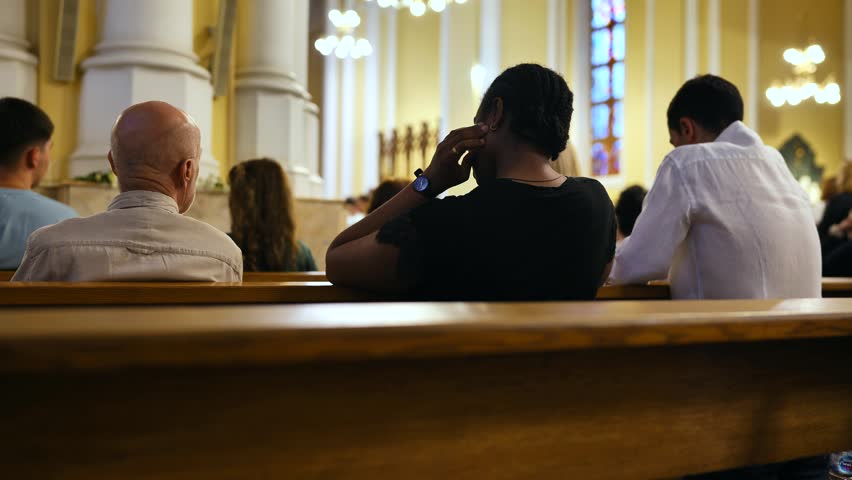People praying and attending religious service in a Catholic Church, rear view