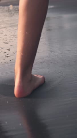 Closeup of feet and barefoot on soft sand at the beach with calm water near the shore, capturing walking along the coastline, wet footprints, and natural textures for lifestyle, travel