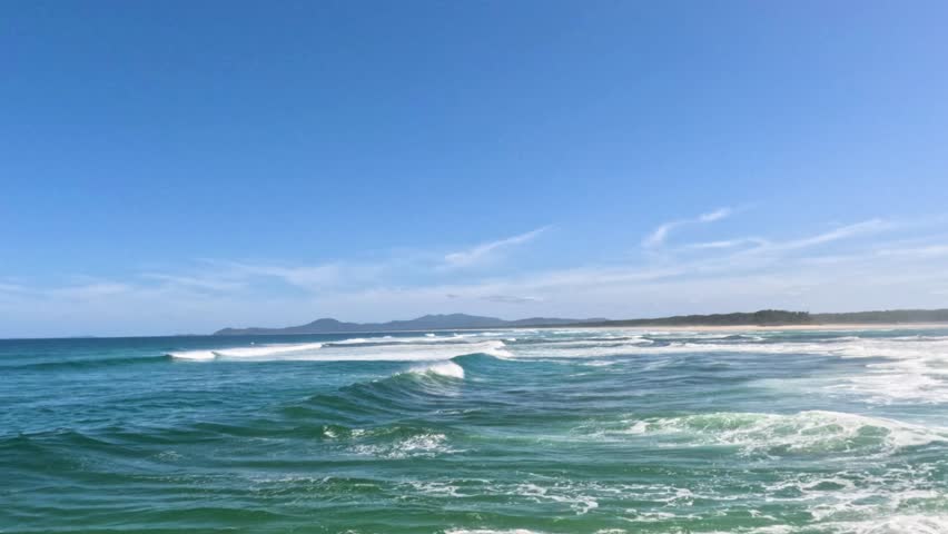Ocean waves rolling in, scenic beach, blue sky, coastal landscape.