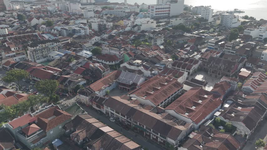 Historic urban preservation and tourism concept: Aerial view of the George Town UNESCO World Heritage Zone in Penang, Malaysia, showcasing traditional red-tile rooftops and heritage shophouses during a bright, quiet morning.